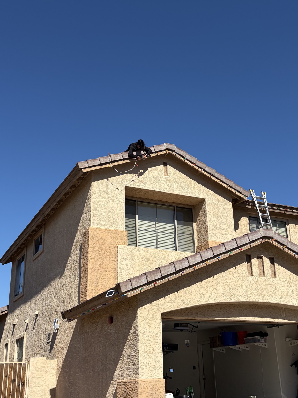 Jodie installing multicolored holiday lights along a two-story home’s roofline